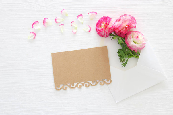 Image of envelope with delicate pastel pink beautiful flowers arrangement over white wooden background. Flat lay, top view. - Foto, afbeelding