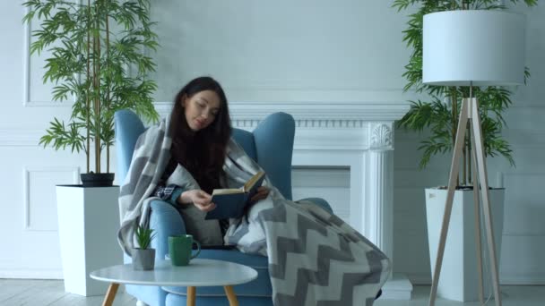 Pretty woman reading a book in armchair at home - Felvétel, videó