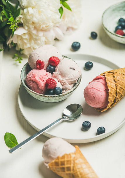 Pink strawberry and coconut ice cream scoops in bowl, sweet cones, peony flowers bouquet and fresh berries over white background - Fotografie, Obrázek
