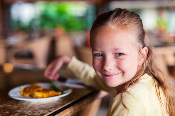 Casual portrait of adorable little girl enjoying meal at restaurant - Фото, зображення