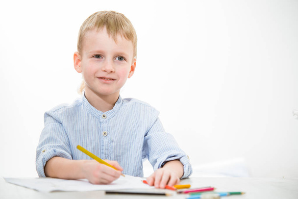Funny boy 6 years old with a pencil sitting at the table in class - Photo, Image