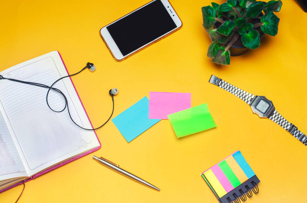 working space with a notebook, pen, clock, telephone, headphones on a yellow background. place for text. The working space of a freelancer, journalist, writer. On a bright yellow background. Top view. - Zdjęcie, obraz