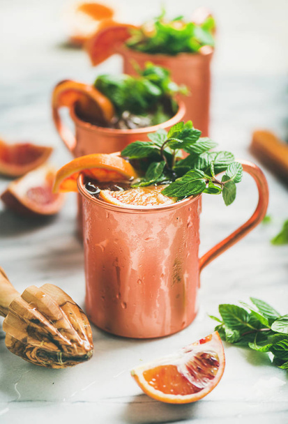 Blood orange Moscow mule alcohol cocktails with fresh mint leaves and ice in copper mugs over white marble background - Photo, image