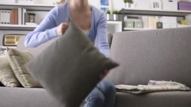 Smiling young woman lying on the sofa at home, she is relaxing and hugging a soft pillow - Imágenes, Vídeo