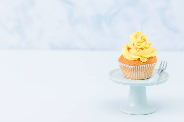 Cupcake con decoración de crema amarilla en soporte vintage sobre fondo pastel azul. Concepto minimalista en la alimentación
. - Foto, imagen