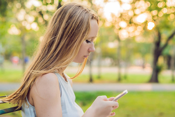 Jeune fille calme utilisant son téléphone portable pour envoyer un message tout en se tenant dans un parc
. - Photo, image