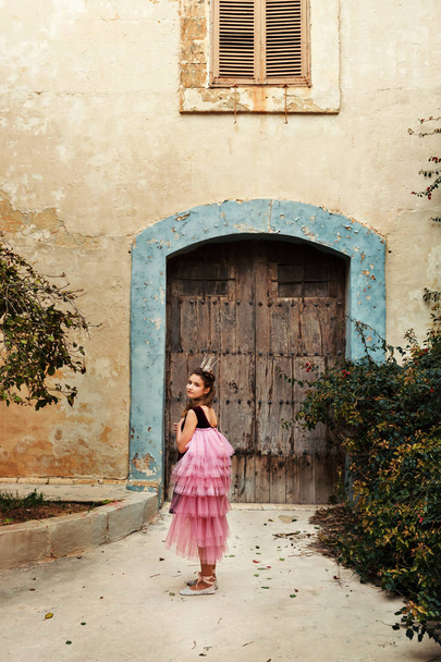a girl in a fairy dress of a princess with a crown turns around walkng to the door of an ancient castle house - Foto, Imagem