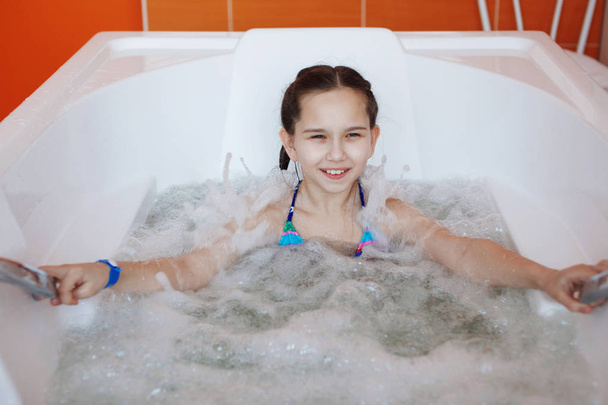 Young little cute teenager girl is sitting in the therapeutic whirlpool bath - Photo, Image
