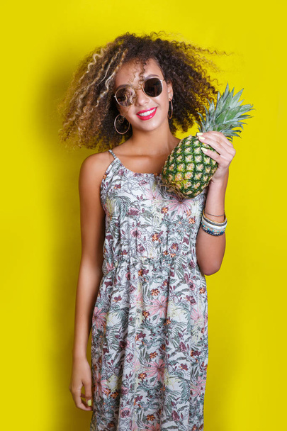 Fashion summer portrait afro american woman in sunglasses and pineapple over yellow background - 写真・画像