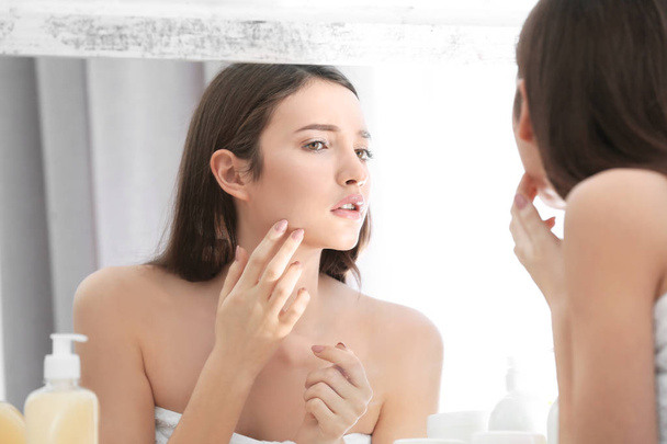 Teenage girl with acne problem looking in mirror indoors - Foto, imagen
