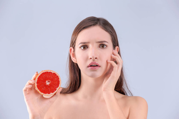 Teenage girl with acne problem holding grapefruit against grey background - Zdjęcie, obraz