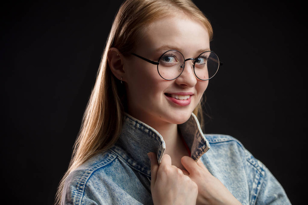 Beautiful girl with blond hair and round glasses looking with a smile at the camera - Zdjęcie, obraz