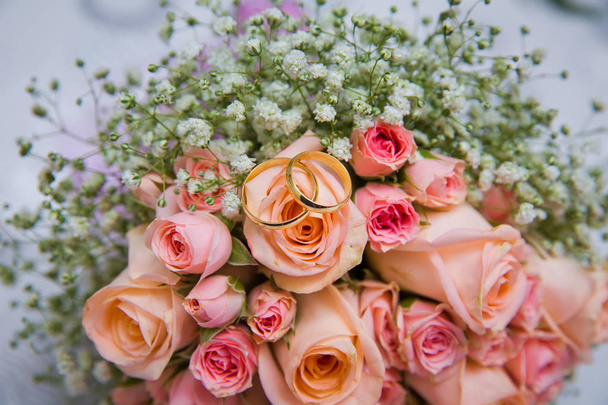 Bridal bouquet with orange and pink roses of different size with handle on white background. Romantic wedding bouquet with beautiful flowers. Two rings represent the meaning of feeling love - Foto, imagen