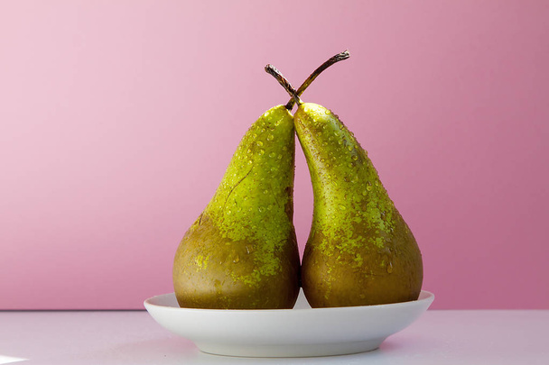 two ripe wet pears on a saucer on a creative pink background - Photo, Image