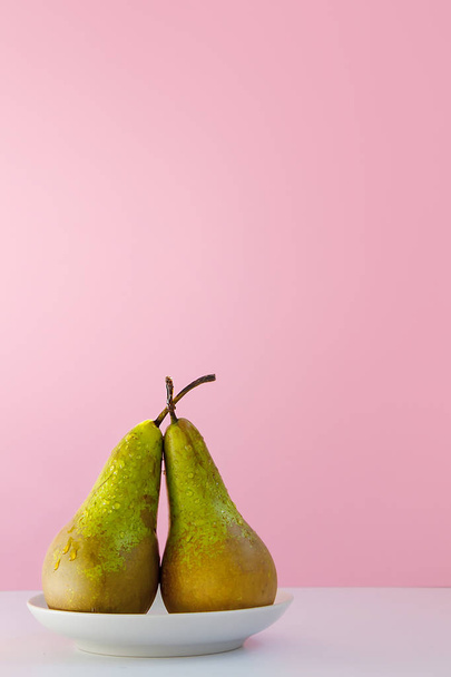 duas peras maduras molhadas em um pires em um fundo rosa criativo
 - Foto, Imagem