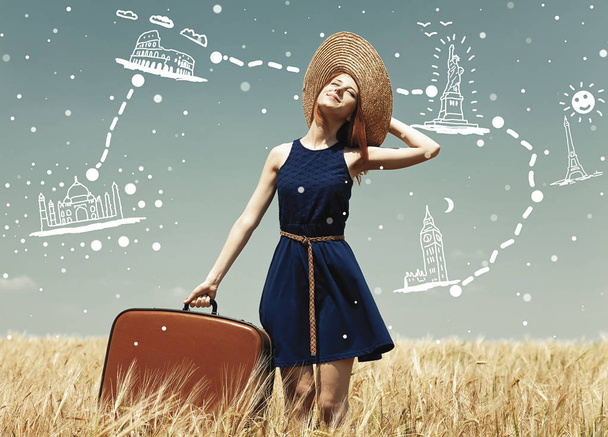κοκκινομάλλα κορίτσι με τη βαλίτσα στο πεδίο σιτάρι άνοιξη. - Φωτογραφία, εικόνα
