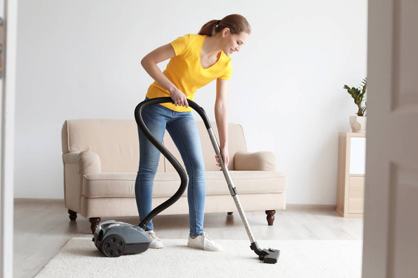 Young woman cleaning carpet with vacuum in living room - Fotografie, Obrázek