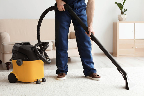 Male worker cleaning carpet with vacuum in living room - Zdjęcie, obraz