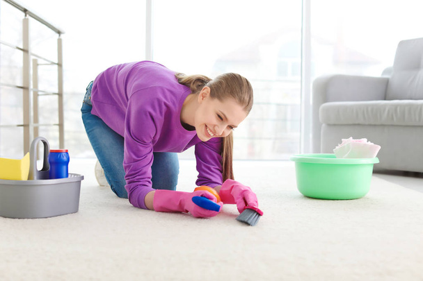 Молода жінка прибирає килим вдома
 - Фото, зображення