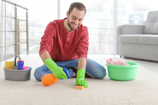 Young man cleaning carpet at home - Fotó, kép
