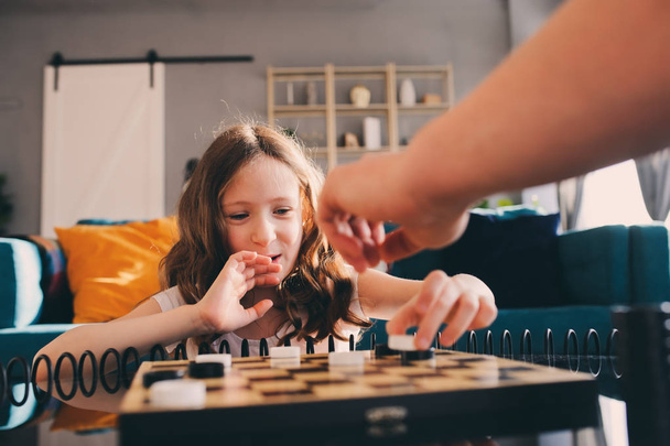 child girl playing checkers with her dad at home. Fatherhood and quality family time concept - Photo, Image