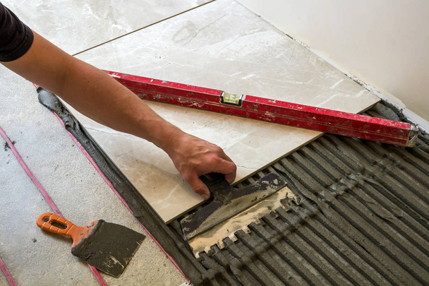 Keramische Fliesen und Werkzeuge für Fliesenleger. Arbeiter verlegen Fußboden  - Foto, Bild