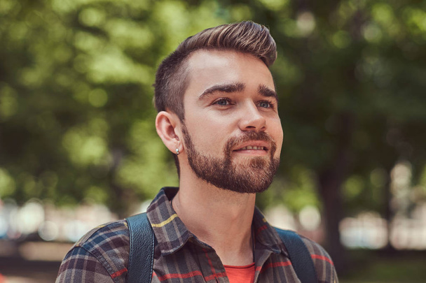 市内の公園に立っているフリースのシャツを着てスタイリッシュな散髪とひげ、若い美しい学生のクローズ アップの肖像画. - 写真・画像