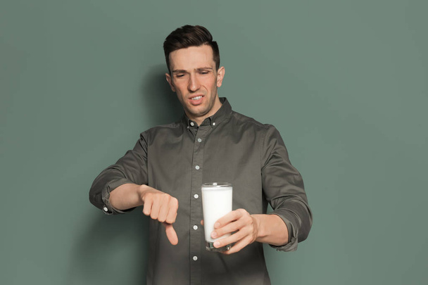 Young man with dairy allergy holding glass of milk on color background - Photo, image