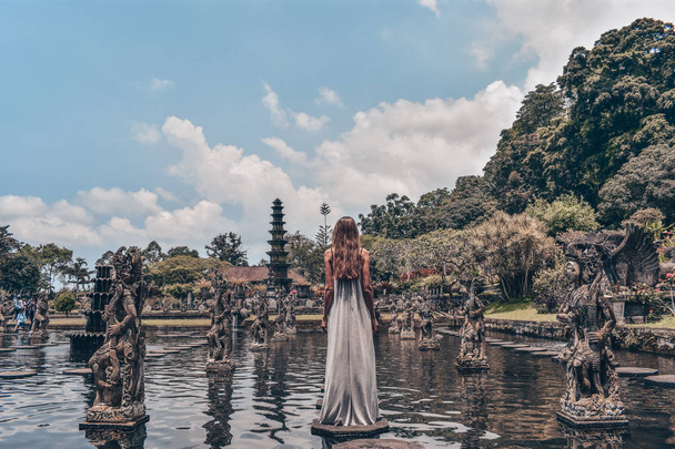 series traveling girl in Asia, beautiful girl with long dark hair in elegant grey dress posing in Tirta Gangga water temple in Bali - 写真・画像