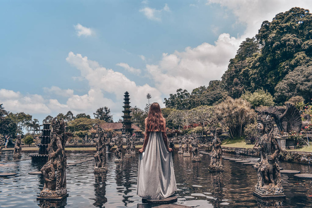серія подорожі в Азії, красива дівчина з довгими темними волосся в елегантному сірий плаття позують Tirta Gangga водного храму на Балі - Фото, зображення