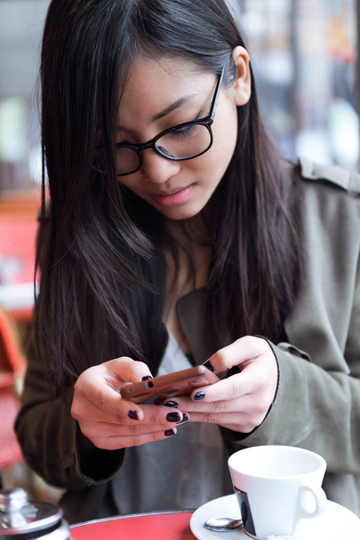 Beautiful young asian woman using her mobile phone in the terrace of a coffee shop. - Photo, Image
