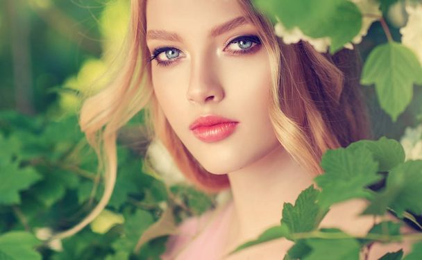 Kaunis kevät tyttö tuoksuva vihreät lehdet. Nainen kukoistavassa puutarhassa. Muoti, kosmetiikka ja hajuvedet. Kiharat vaaleat hiukset
 - Valokuva, kuva