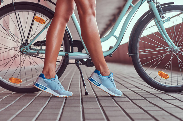 Immagine ravvicinata di gambe femminili sottili lisce in una sneakers blu vicino alla city bike
. - Foto, immagini
