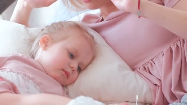 Little charming blond girl plays with baloon with her mom in pink dress laying on bed. - Video, Çekim