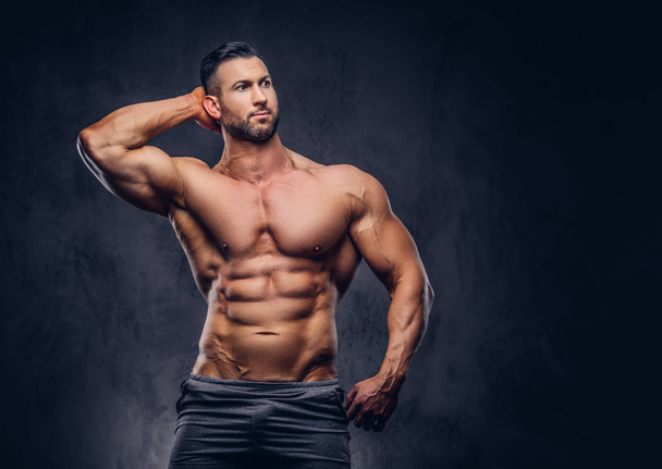 Portrait of a shirtless tall huge male with a muscular body with a stylish haircut and beard, in a sports shorts, posing in a studio. Isolated on a dark background. - 写真・画像