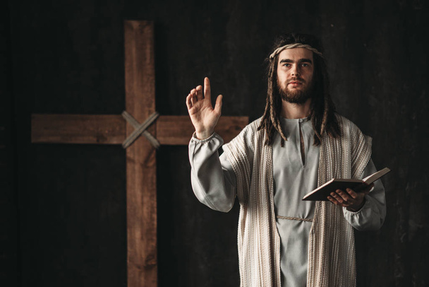 Święty Jezusa Chrystusa modląc się z Biblią w ręce, krzyż na czarnym tle - Zdjęcie, obraz