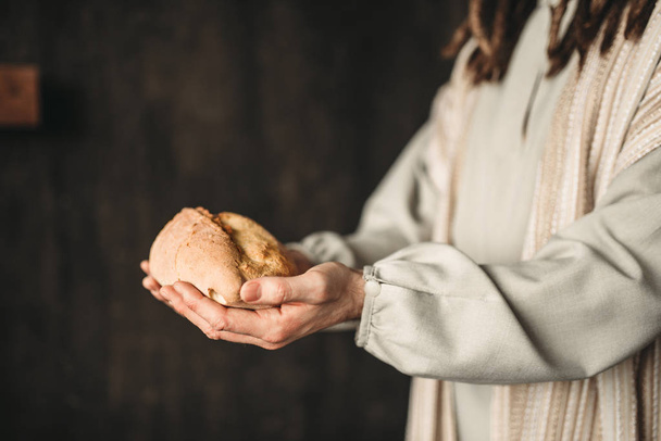 Jesus Cristo com pão nas mãos, comida sagrada, cruz de crucificação no fundo
 - Foto, Imagem