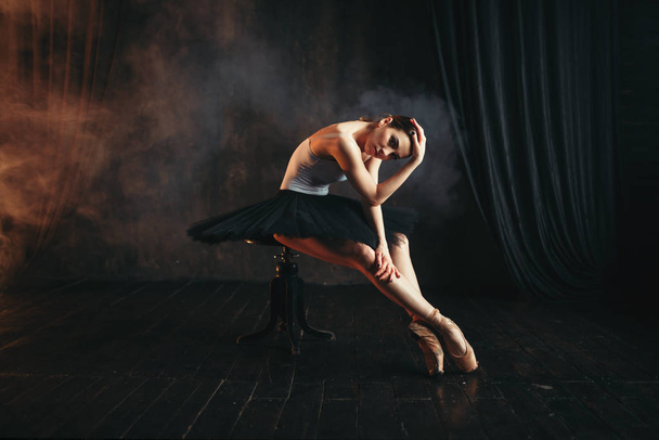 витончена і красива балерина сидить на чорній банкеті на сцені театру
 - Фото, зображення