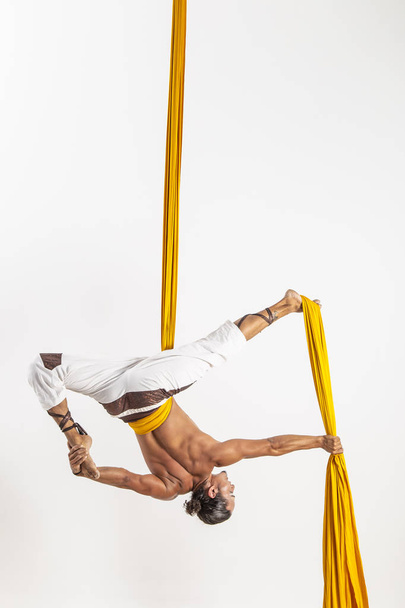 vonzó izmos ember csinál akrobatikus teljesítményt, fehér alapon sárga szövet - Fotó, kép