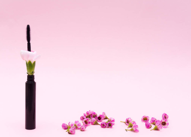 Black mascara decorated of small flowers. Creative style organic cosmetics background. Beige soft color romantic design. Use for advertising - Photo, Image