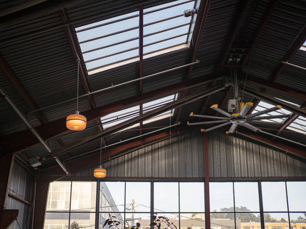 Teollisuuden tuuletin ja ikkunat korkea katto varastossa aurinkoisena päivänä
 - Valokuva, kuva