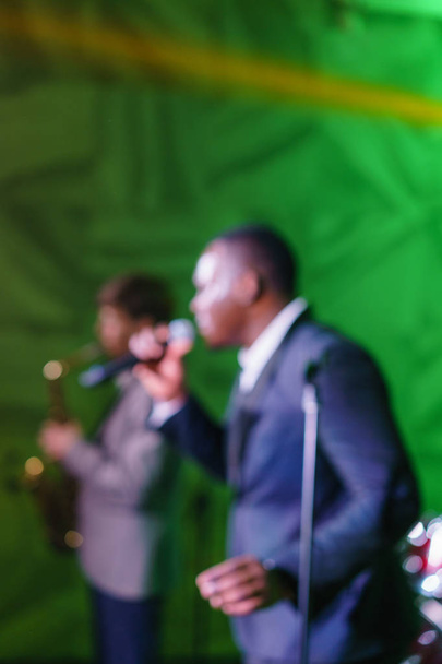 Анотація розмиття. Афро американський людина співає в мікрофон. Джазовими музикантами, виступати на сцені в клубі перед натовпом cheering - Фото, зображення