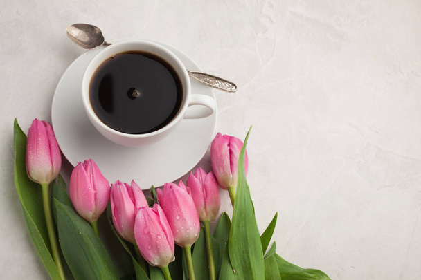 Czarna kawa w białe filiżanka z różowe tulipany na jasnym tle kamienia. Widok z góry z miejsca kopii - Zdjęcie, obraz