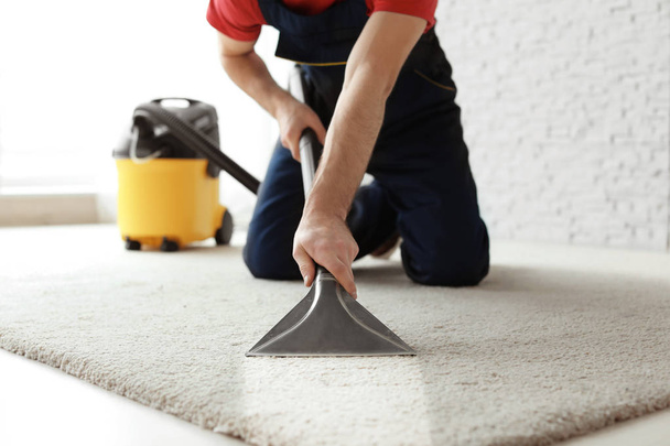 Male worker cleaning carpet with vacuum indoors - Foto, Imagem