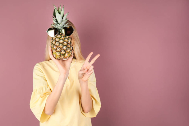 Woman holding pineapple with sunglasses on color background - Fotografie, Obrázek