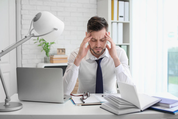 Man suffering from headache while sitting at table in office - Valokuva, kuva