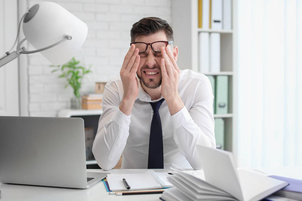 Man suffering from headache while sitting at table in office - Fotoğraf, Görsel