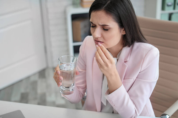 Young woman taking pill against headaches while sitting at table in office - Фото, изображение