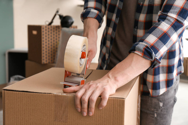 Молодий чоловік упаковує рухому коробку в приміщенні, крупним планом
 - Фото, зображення