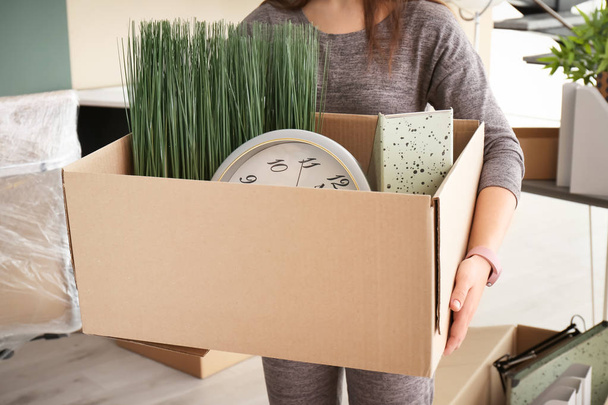 Young woman holding moving box with office stuff indoors, closeup - Foto, afbeelding